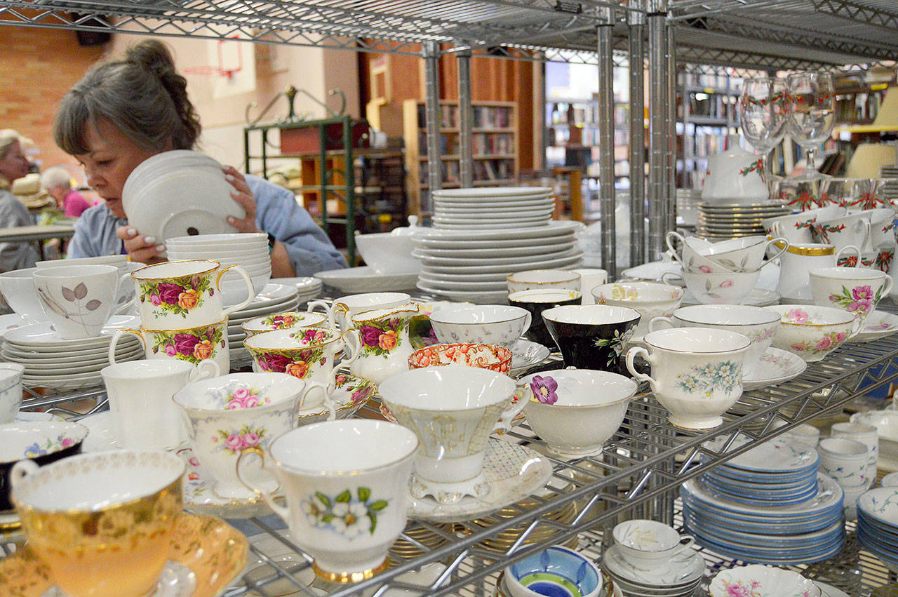 Lion Deanna Rogers organizes shelves of china. Among the dishware for sale is a 16-place setting set of Johann Haviland-Baravia dinnerware in the retired Cinnamon Rose pattern. Photo by Megan Hansen/Whidbey News-Times