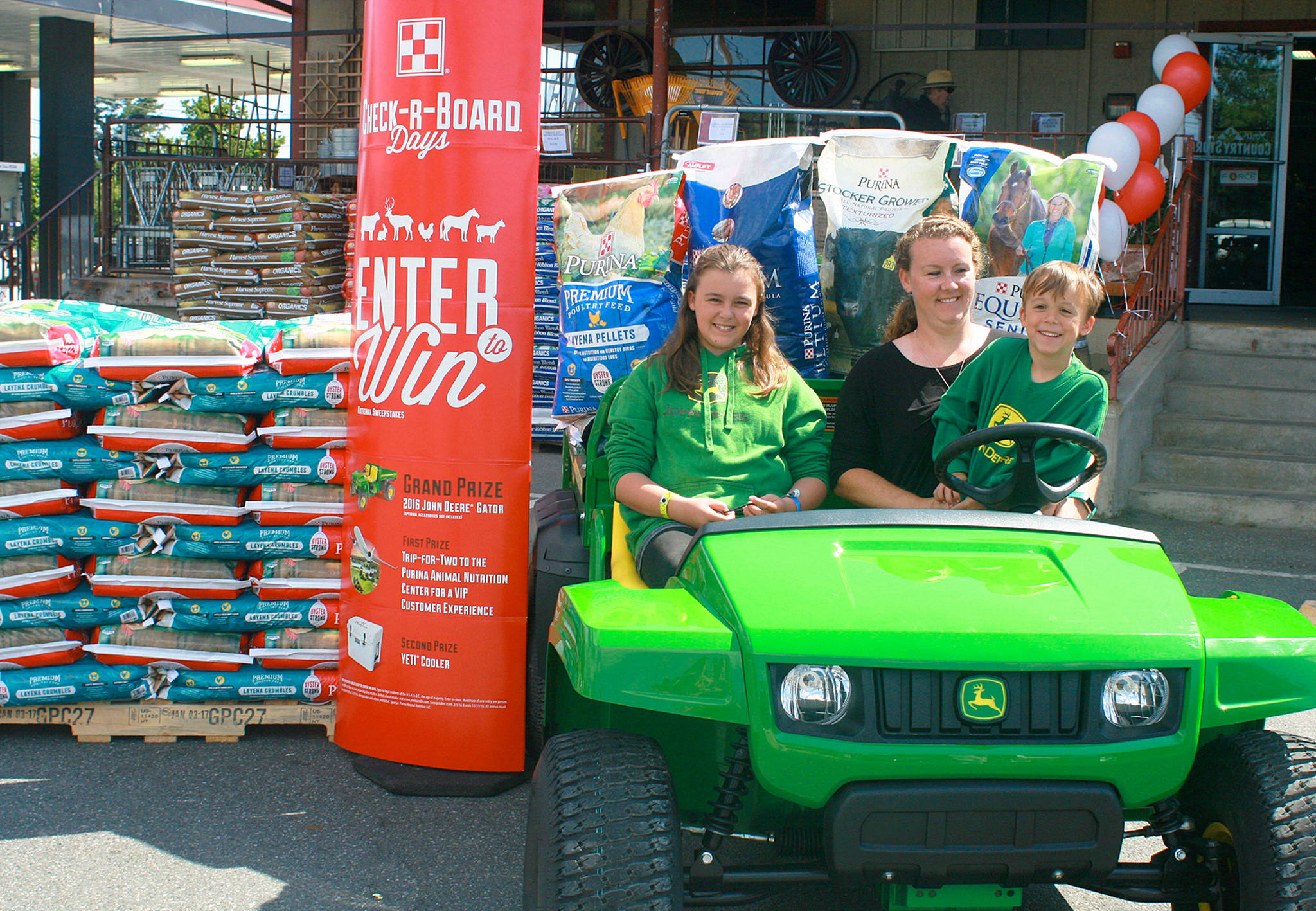 From left, Linndsy, Jenn and David Scheer get a feel for their new John Deere ATV as grand-prize winners of Purina Check-R-Board Days’ national sweepstakes, last week at the Oak Harbor Country Store. Photo by Daniel Warn/Whidbey News-Times