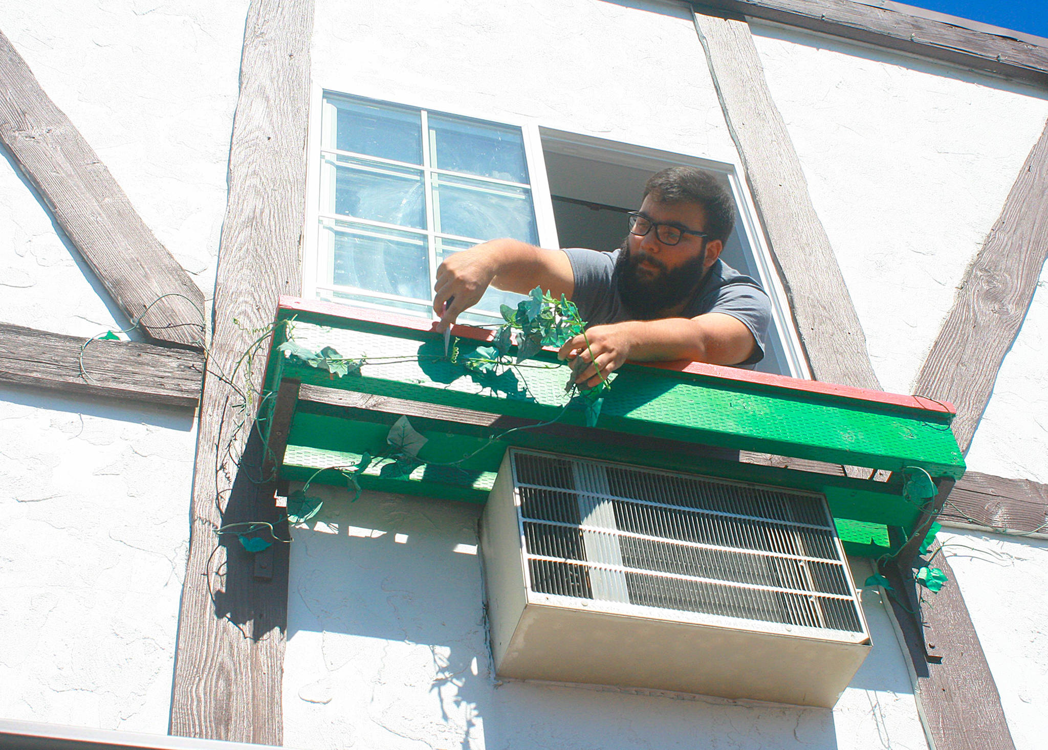 Narno Loza, maintenance worker and housekeeper for Auld Holland Inn, hangs out of a second-story window as he removes worn flower decorations to spruce the place up Monday morning. Photo by Daniel Warn/Whidbey News-Times