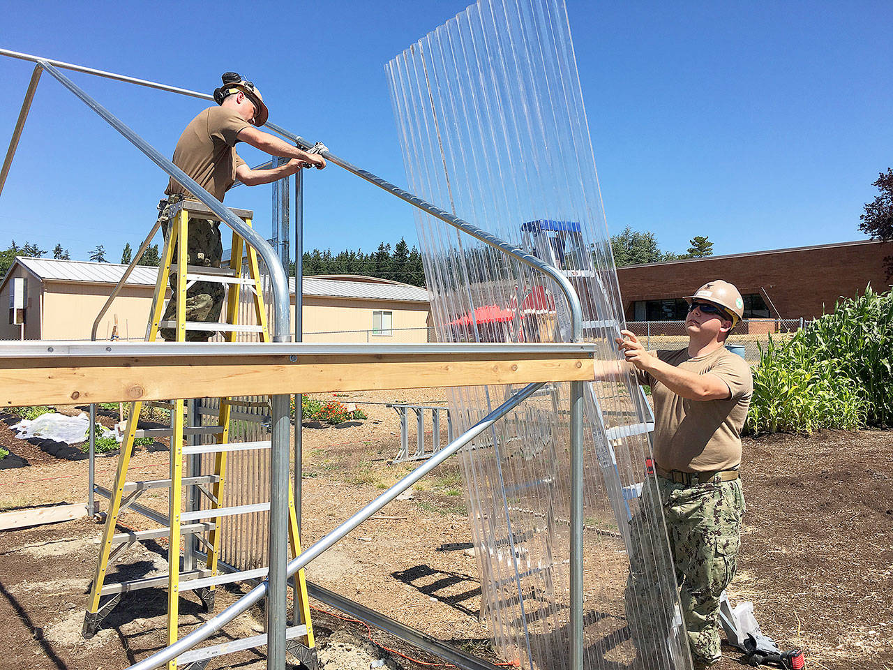 U.S. Navy Petty Officer Second Class Colt Wilson, left, and Petty Officer Joseph Puls attach greenhouse plastic to Crescent Harbor Elementary’s new hoop house Wednesday.Photo by Daniel Warn/Whidbey News-Times