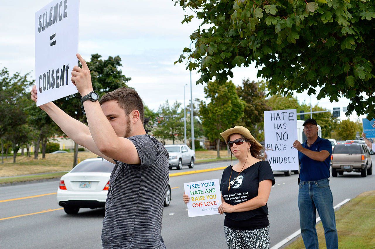 Lori Taylor, her husband Jim Colton (right) and her stepson Ben Colton (left) show signs to passing cars during an assembly against racism Friday outside of Big 5 in Oak Harbor. Taylor organized the event in response to the Equal Employment Opportunity Commission’s lawsuit against the company. Photo by Laura Guido/Whidbey News-Times