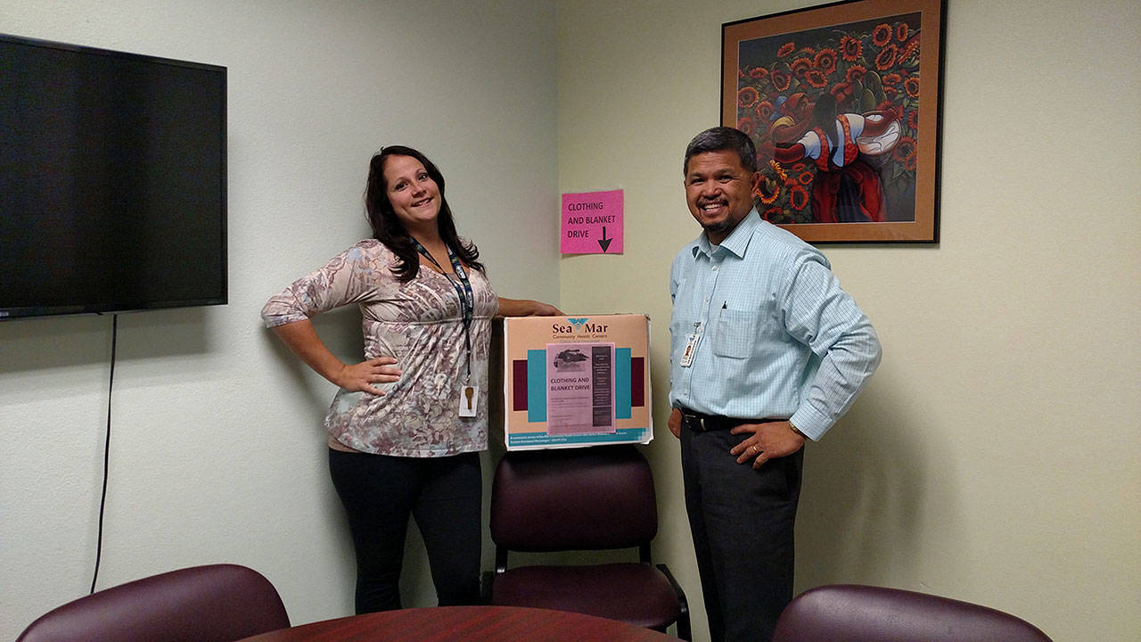Christin McCausland (left) and Emmanuel Montenegro stand next to one of the donation boxes for SeaMar Community Health Center’s blanket and clothing drive. Photo provided by SeaMar