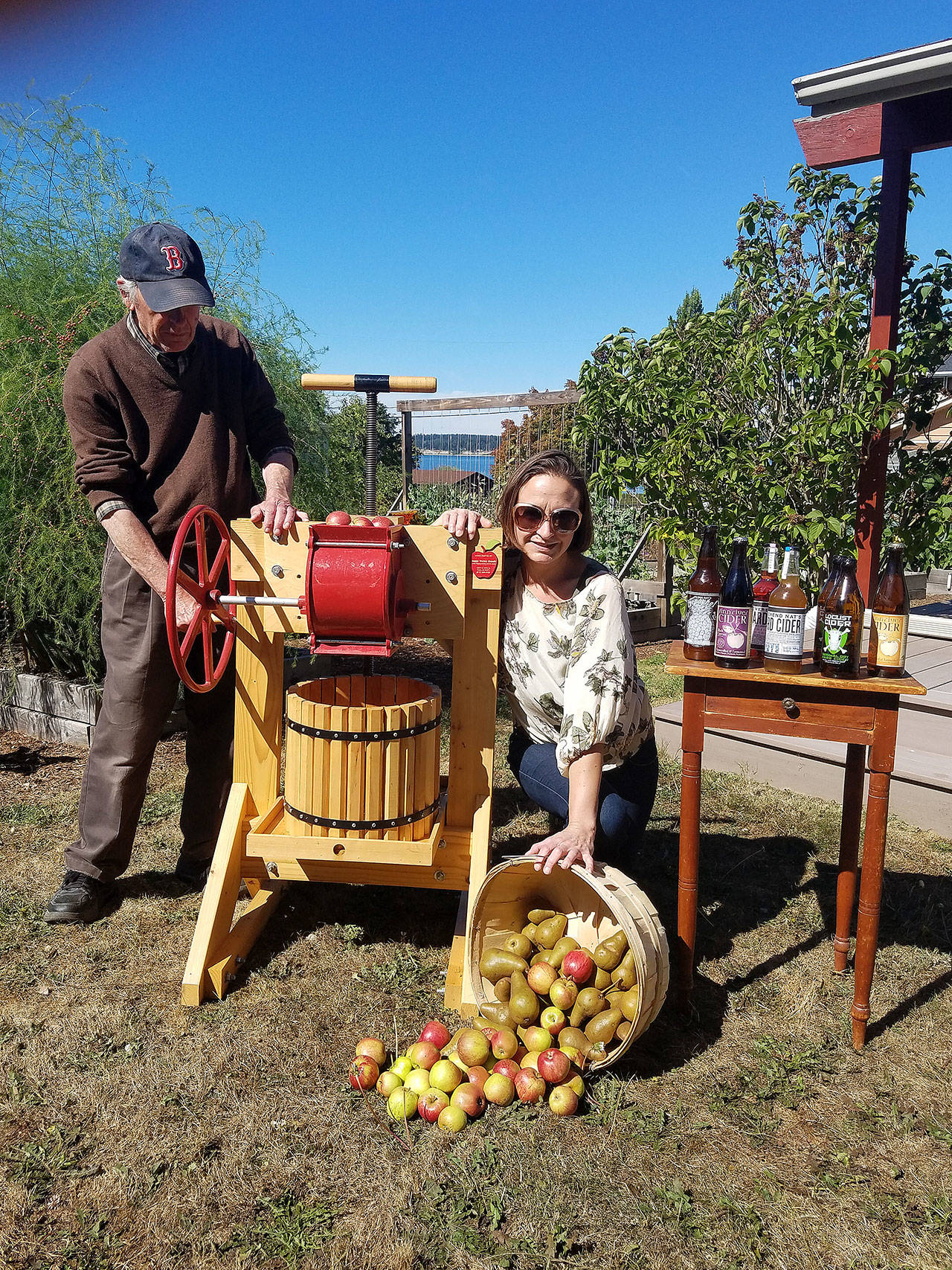 Coupeville resident Jay Adams will be loaning his vintage apple press to next Saturday’s Cider Festival at Pacific Rim Institute. Mosa Neis with PRI shows off the bushels of apples and variety of cider available for tasting. Photo by Patricia Guthrie/Whidbey News-Times.