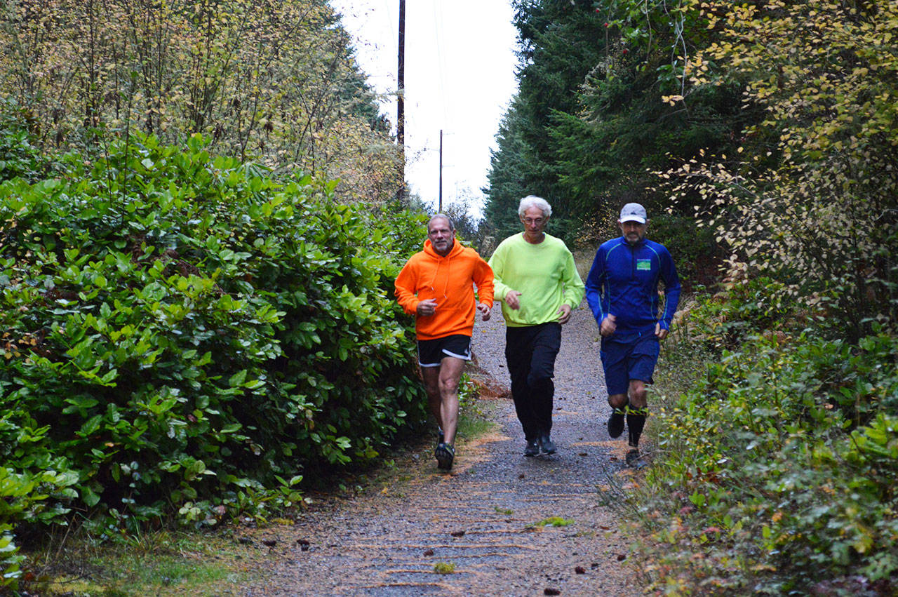 From left, Fran Einterz, Wilbur Bishop and Noah Landau jog down the Kettles Trail. All three have been attacked by an owl at least once. Photo by Laura Guido/Whidbey News-Times