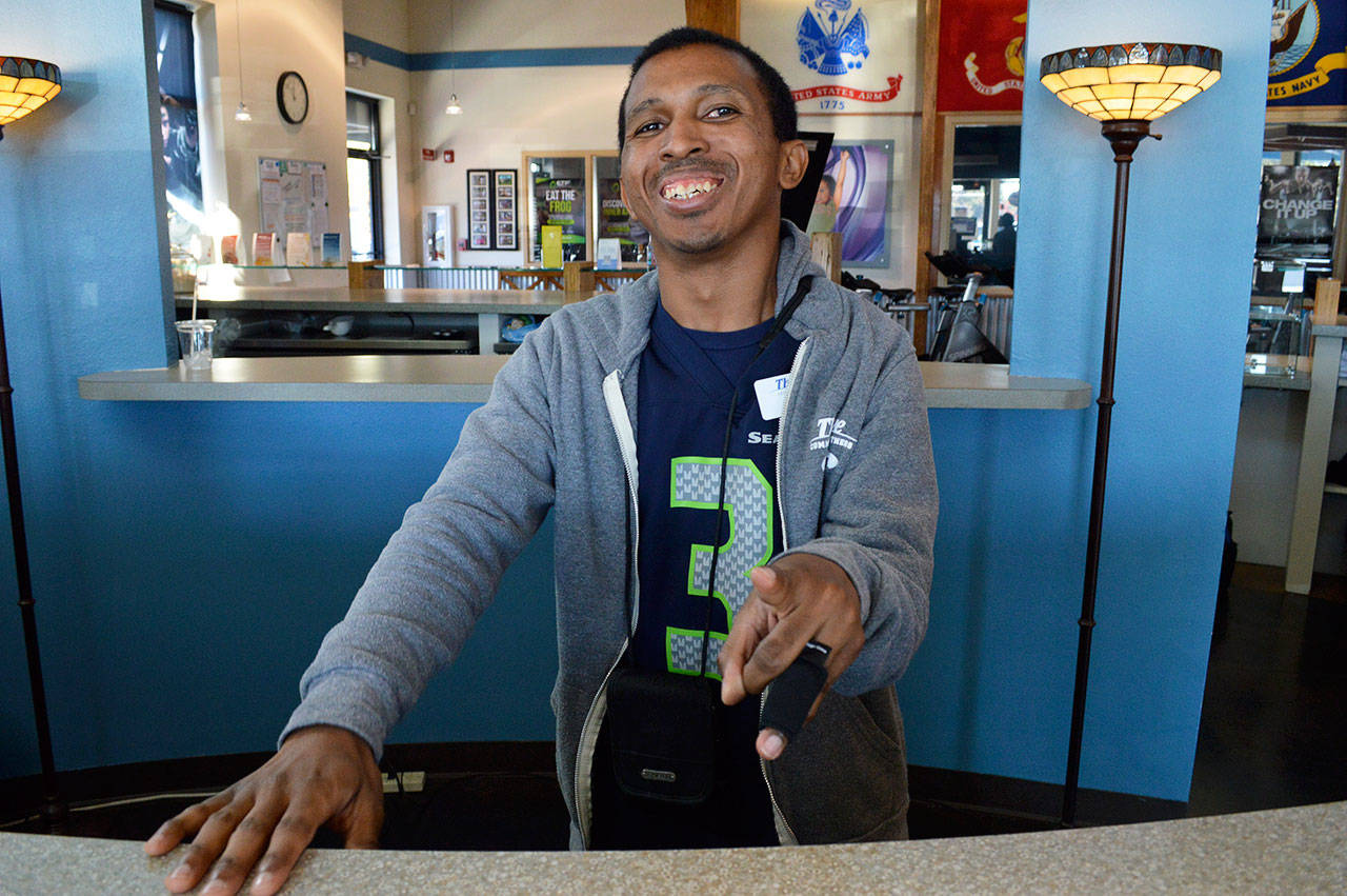 Geno Dogans shows the camera his “E.T.” finger as he stands behind the counter at Thrive Community Fitness. He uses his amiable personality to make customers feel welcome as they walk in; he got his job there through the county’s work program for adults with developmental disabilities. Photo by Laura Guido/Whidbey News-Times