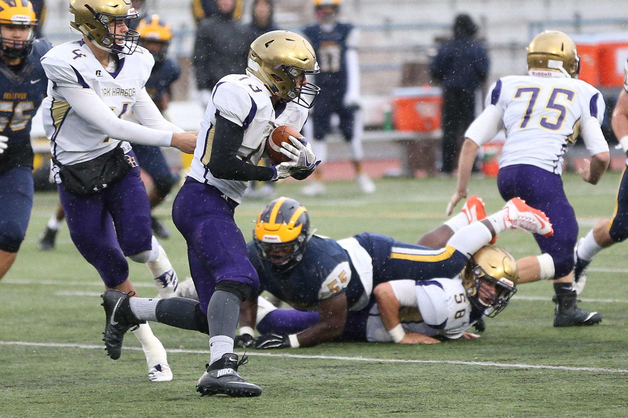 Oak Harbor quarterback Jordan Bell (4) hands off to Aaron Martinez as Brandon McCollough (58) and Hunter Bos (75) provide a running lane.(Photo by John Fisken)