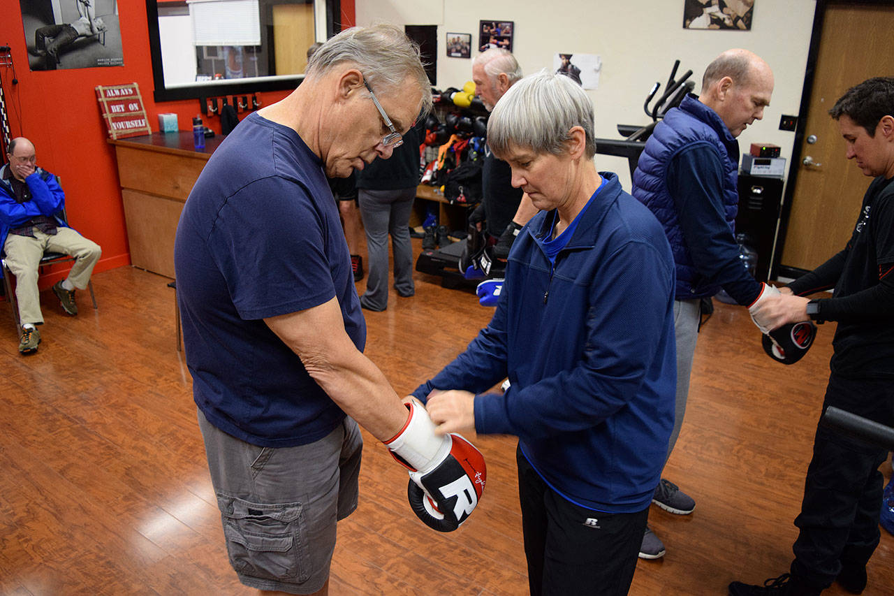 Kyle Jensen / The Record — Trainer Sue Taves helps a boxer put on his gloves before the session starts. Taves doesn’t have a background in boxing, but was brought into the program as a physical therapist.