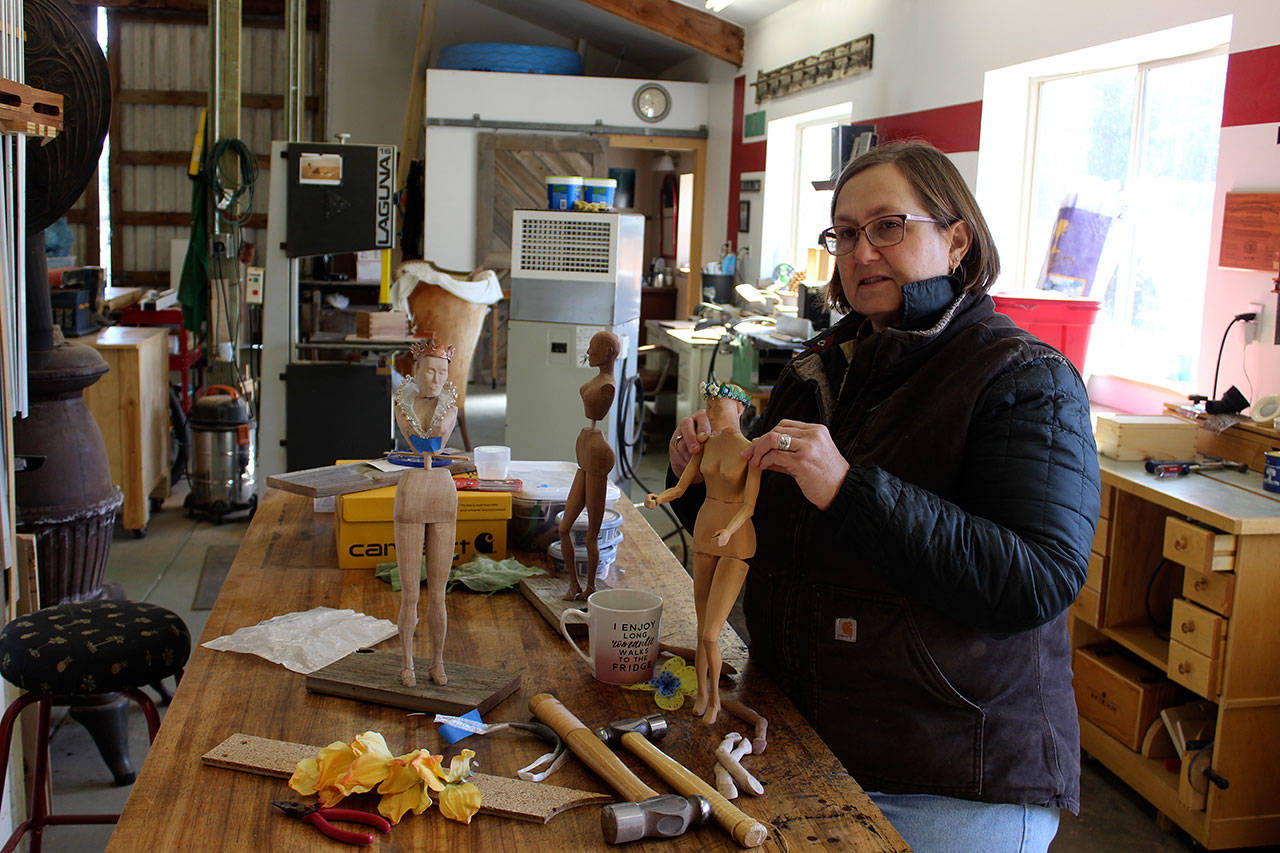 Janet Lewis, a woodworker, carved three Shakespearean female figures from scrap wood. She’s adorning them with old fake flower petals, bottle caps and jewelry, reused feed bags and coiled wire for curly hair. Photo by Patricia Guthrie/Whidbey News-Times