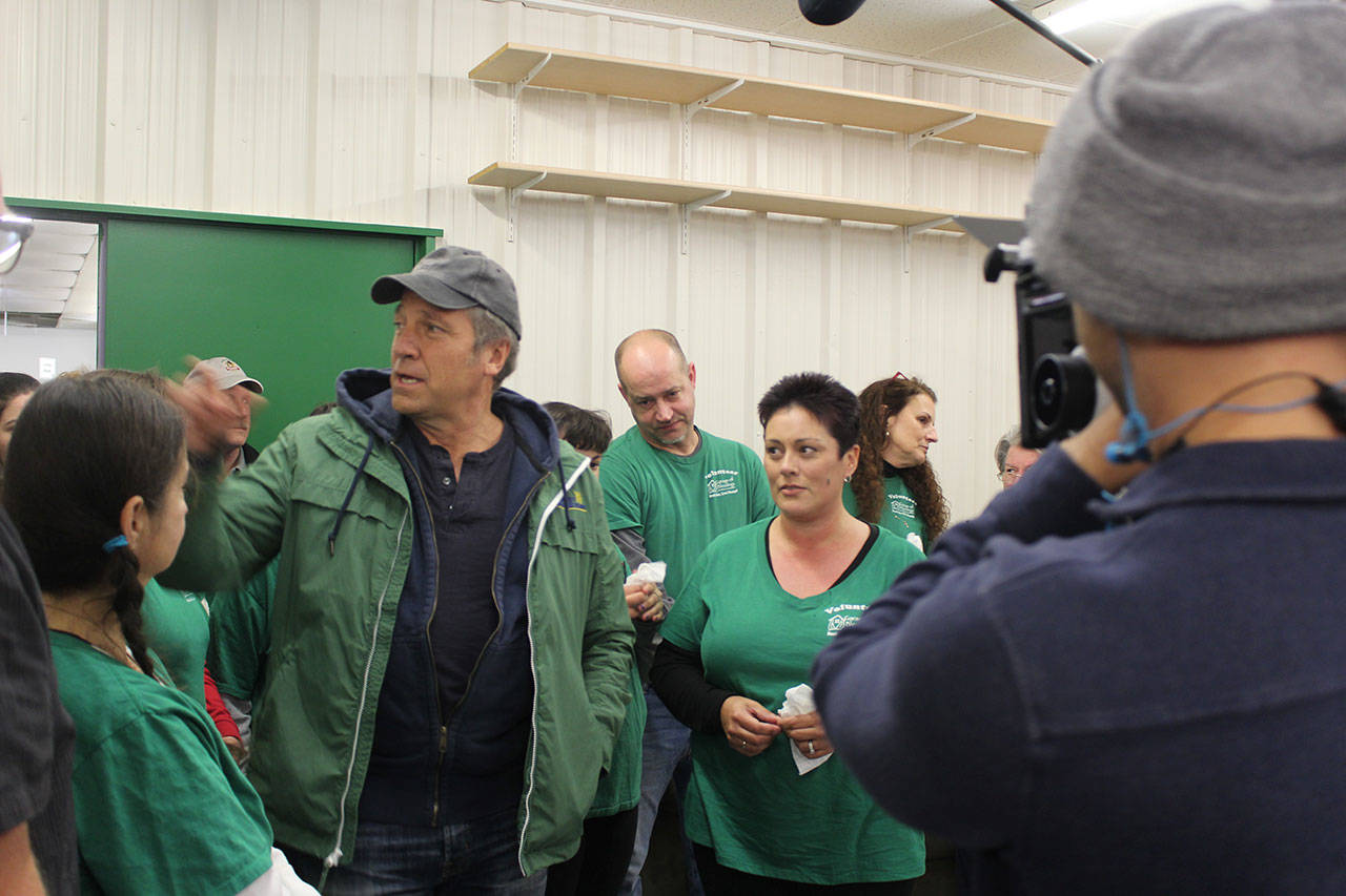 Garage of Blessings and founder Kristiina Miller (center) takes Mike Rowe (left) on a tour of the nonprofit. Rowe surprised Miller with money, an expanded renovated space, new office and a van in November. They are being filmed for the Facebook series, Returning the Favor. The episode aired recently.