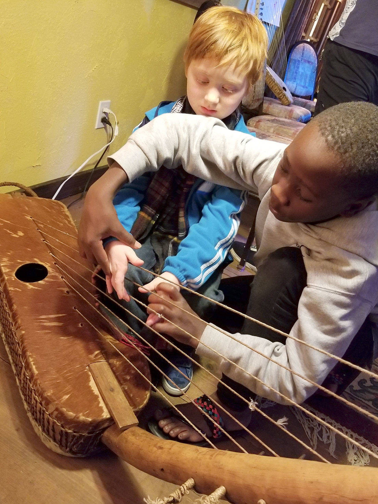 Erick Ngabezaaya (right) shows where to properly place fingers on the Ugandan wooden instrument called an adungo to Shane Astor of Everett.