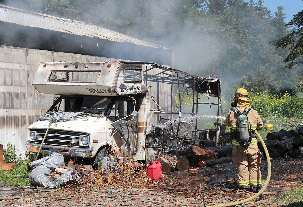 Photo by Jessie Stensland / Whidbey News-Times                                A firefighter sprays down an RV that caught fire at a North Whidbey home Tuesday.