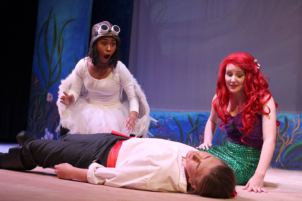 Ella Langrock is Ariel, a love-struck mermaid with a golden voice. She kneels over knocked-out Eric, a prince played handsomely by Griffin Stein. Her feathered friend, Scuttle, played by Miranda Abunimeh, is shocked at what washes up on the beach. Photo by Patricia Guthrie/Whidbey News Group