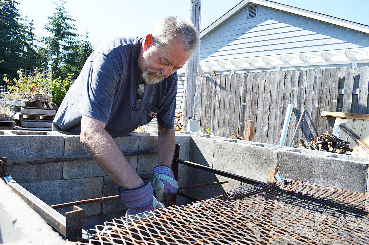 John Ryan demonstrates how the pig butt meat will be skewered to be able to fit more in the large cinder block pit he made for Oak Harbor Pigfest. He and other festival organizers will smoke 4,000 pounds of pork in a pit that will include three additions to the one pictured. Photo by Laura Guido/Whidbey News-Times