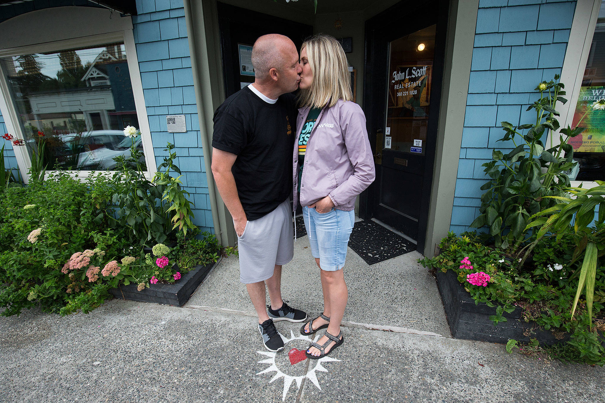 Theron Murphy, of Orem, Utah, kisses his wife, Jody, in front of the John L. Scott Real Estate office in Langley. People stand on the sidewalk on the heart, kiss, then make a hash mark on the chalkboard. The office keeps a tally and posts the monthly and yearly count. (Andy Bronson / The Herald)