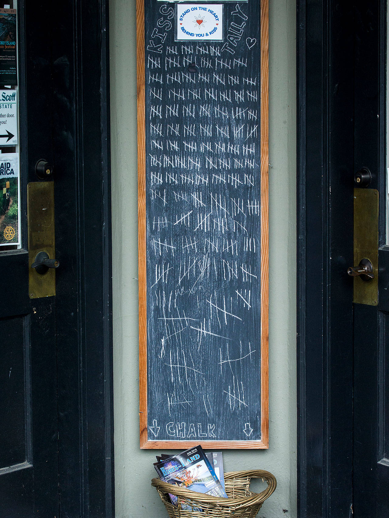 Tally marks get longer and messier the further down a chalkboard in front of the John Scott Real Estate office on First Street in Langley. Visitors to Langley can stand on the sidewalk on the heart and kiss, then make a hashmark on the chalkboard. The office keeps a tally and posts the monthly and yearly count. (Andy Bronson / The Herald)