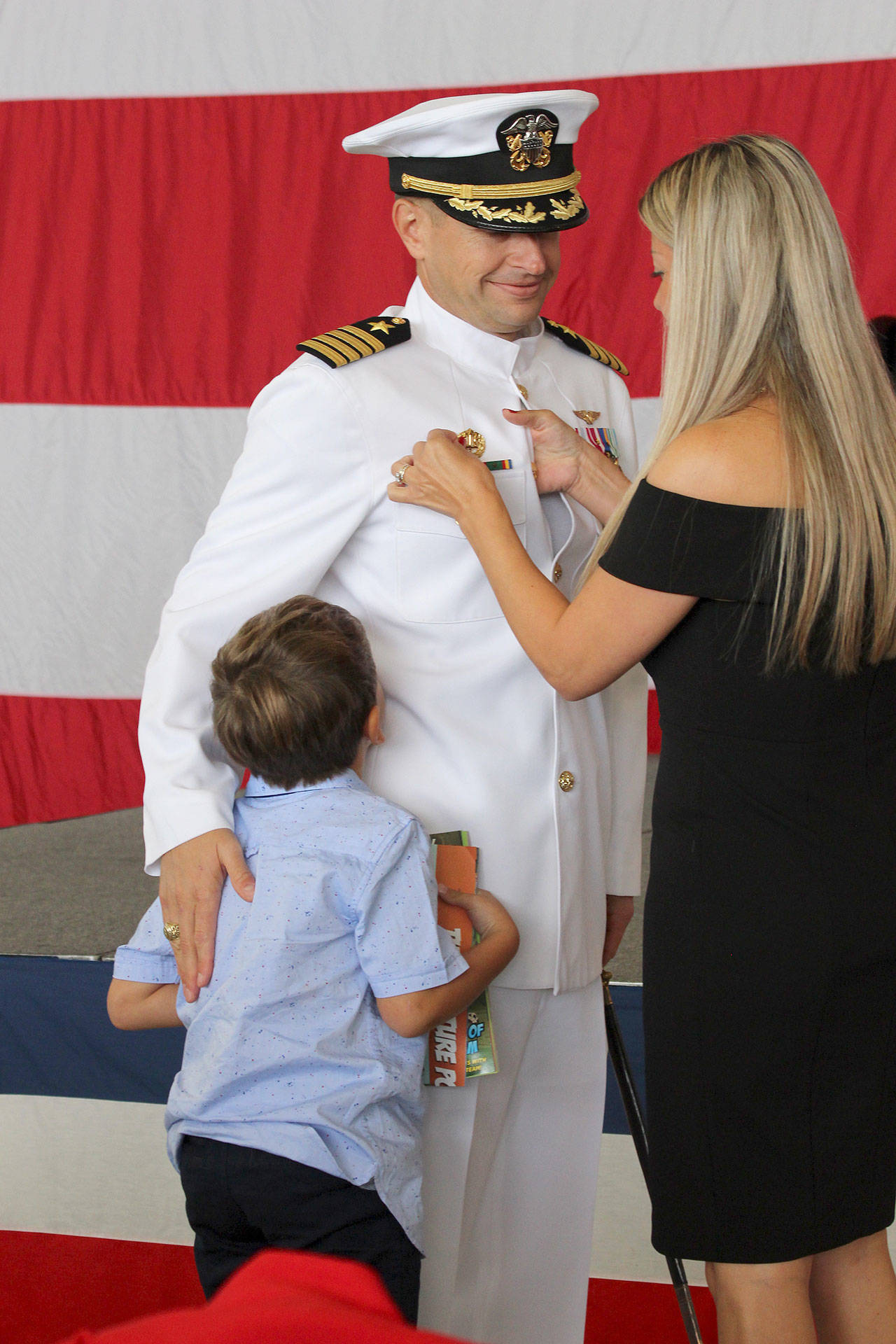 Photo by Maria Matson / Whidbey News Group                                Capt. Matthew Arny smiles as his wife Samar pins a command pin to his uniform and one of his two sons looks on.