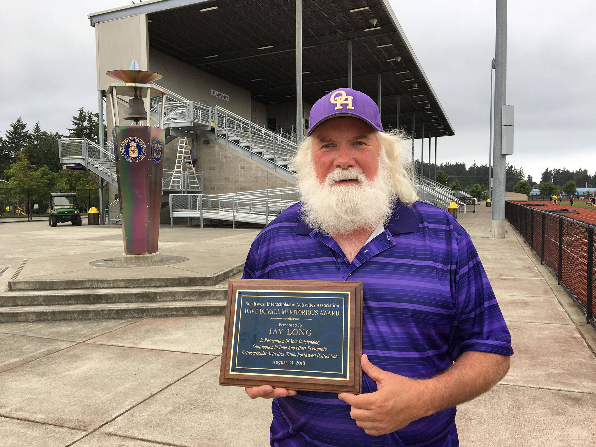 Jay Long displays his Dave DuVall Award in front of Wildcat Memorial Stadium where he volunteers as the public address announcer. (Photo by Jim Waller/Whidbey News-Times)