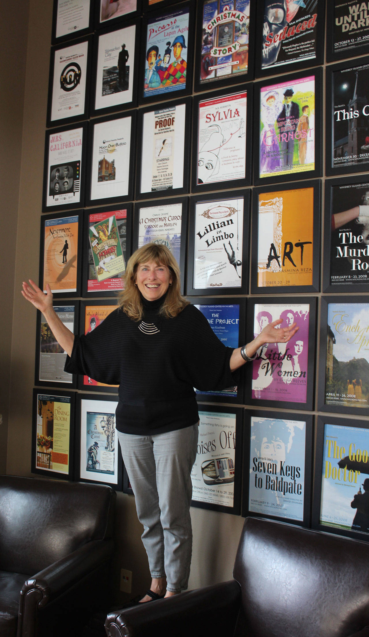 Stacie Burgua, outgoing executive director of Whidbey Island Center for the Arts, stands in front of posters from the more than 75 theater productions staged during her 18-year tenure. (Photo by Patricia Guthrie/Whidbey News Group)
