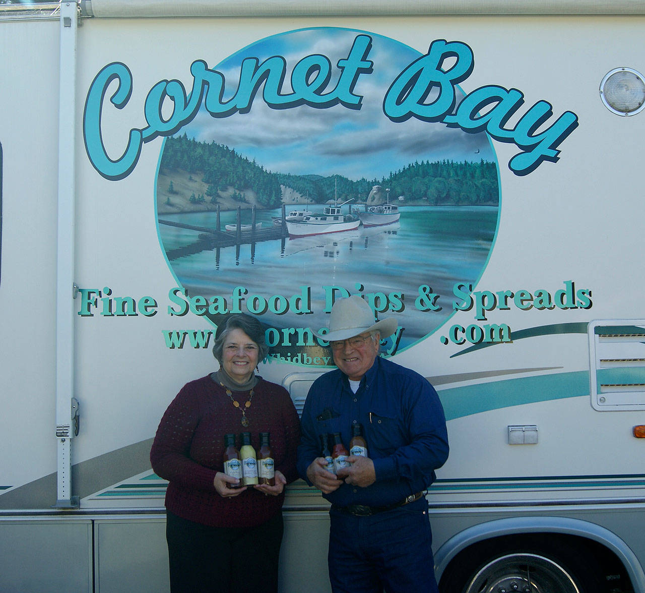Photo by Maria Matson/Whidbey News Group.                                &lt;em&gt;Cornet Bay Company owners Arnie and Joanne Deckwa stand with their new seafood line of sauces. In the background, painted on their RV is the company’s logo depicting Cornet Bay, the view across from their office.&lt;/em&gt;