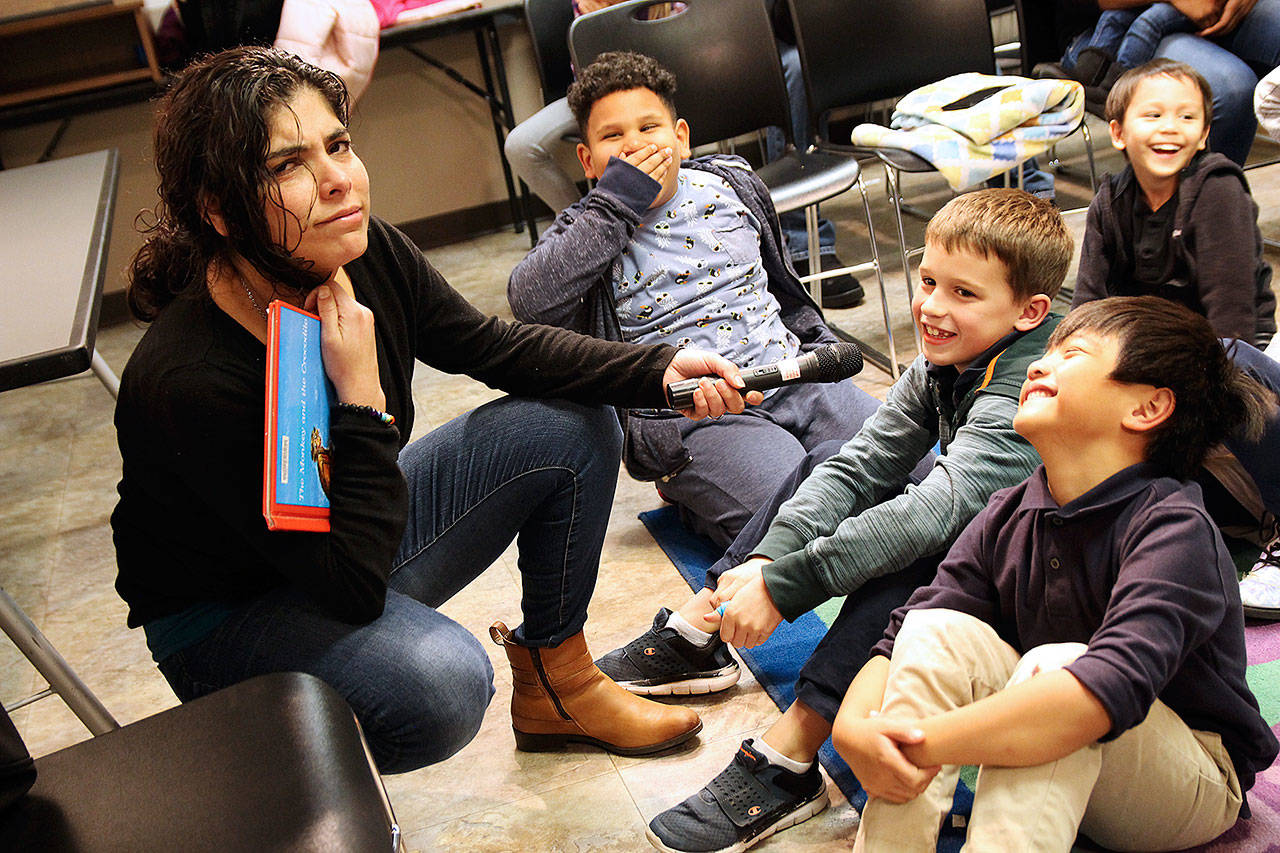 Volunteer reader Claudia Sámano Losada reacts to an answer given by Grayson Wolniakowski, center, Tuesday night at Oak Harbor Library’s Prime Time reading program. Jaime Abreu Serrano, left, and Josh Matro giggle in response. Photo by Laura Guido/Whidbey News-Times
