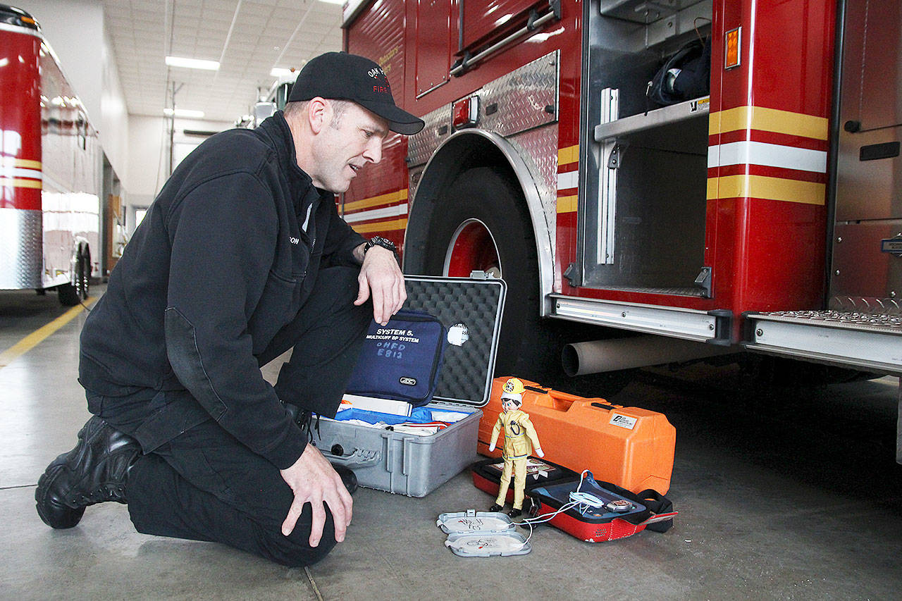 Fire Capt. Craig Anderson and Simon the elf go over how to use an automatic external defibrillator, or AED. Photo by Laura Guido/Whidbey News-Times