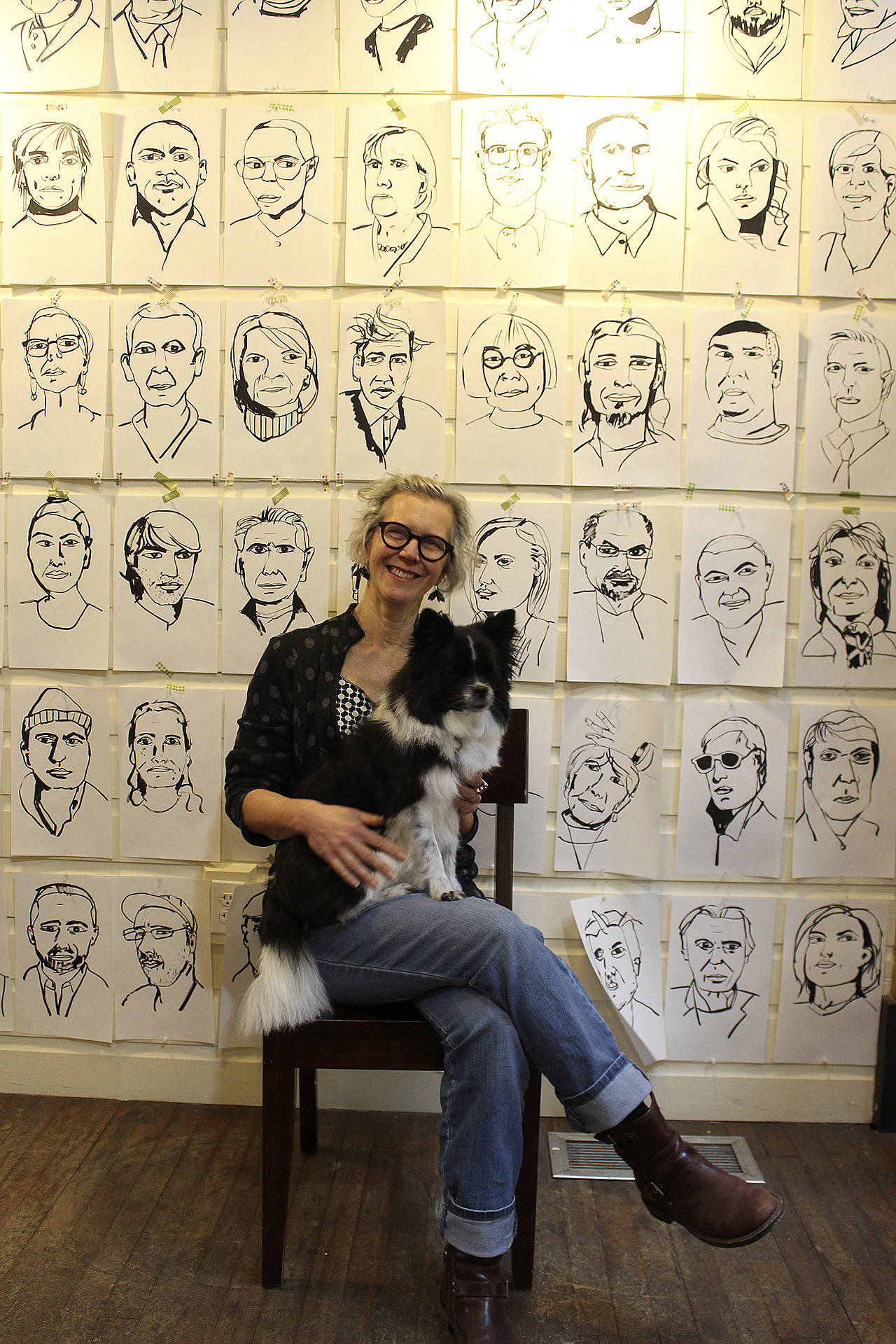 Meredith MacLeod poses with Mica at Bayview Cash Store in front of some of her portraits. Wednesday, Jan. 1 from 4 to 6 p.m., she’ll be talking about the response to her interactive exhibit, “First Impressions.” (Photo by Patricia Guthrie/Whidbey News Group)