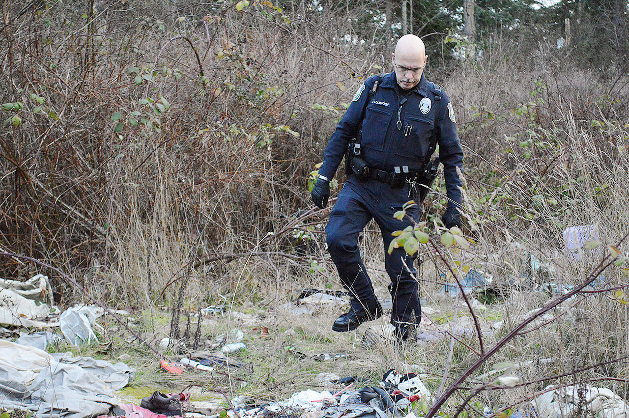 Officer Mel Lolmaugh, Oak Harbor Police Department, carefully steps over the trash in an area known as The Pit off of Goldie Road. Photo by Laura Guido/Whidbey News-Times