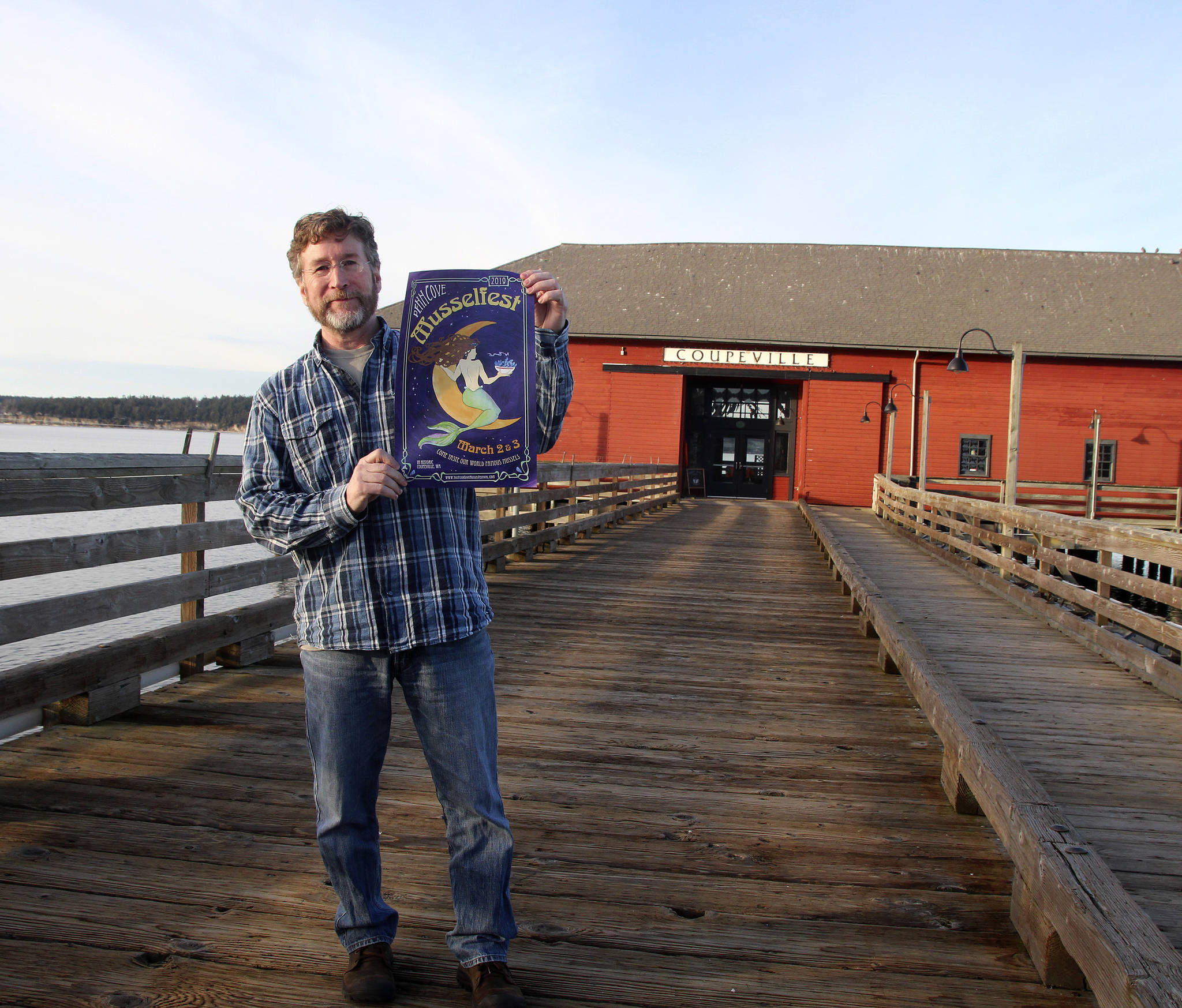 Scott Rosenkranz holds up his design for the 2019 Musselfest poster. The festival will be held March 2-3 in Coupeville. (Photo by Maria Matson/Whidbey News-Times)
