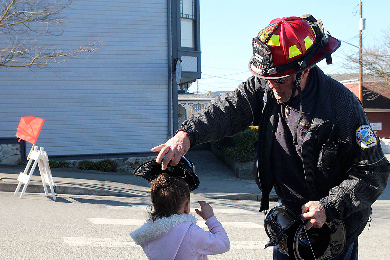 Firefighter Lieutenant Bob Moore of Central Whidbey Fire and Rescue places a plastic helmet on the head of a young visitor. (Photo by Maria Matson/Whidbey News -Times)