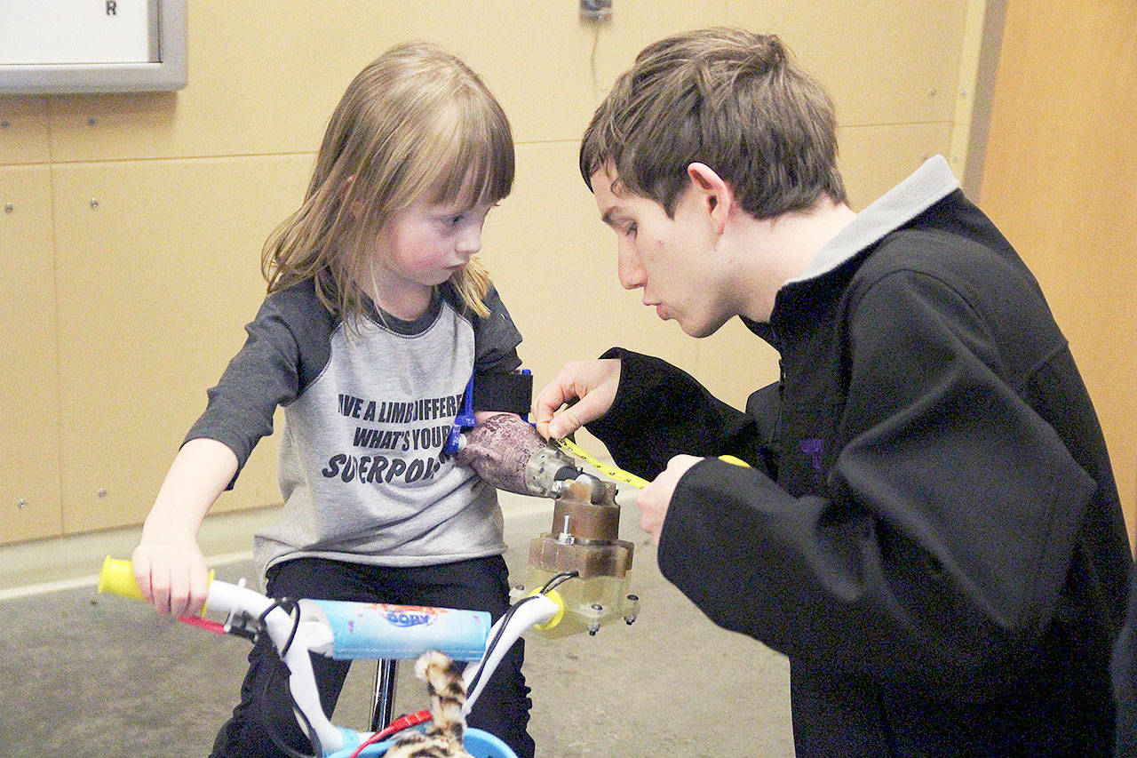 Oak Harbor High School senior Logan Ince measures an arm cuff for 4-year-old Michaela Reed to help her steer a modified bike. (Photo by Laura Guido/Whidbey News-Times)