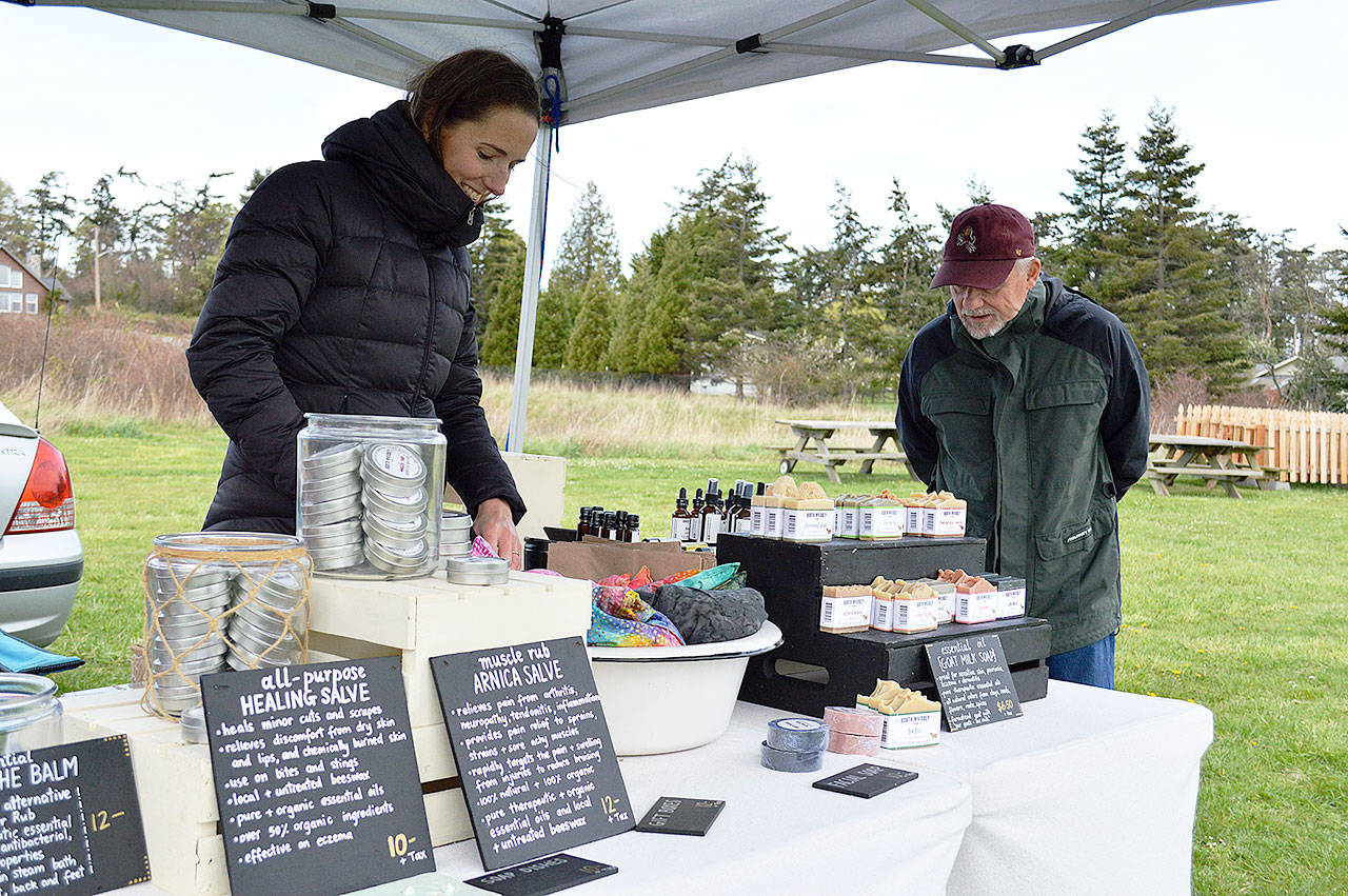North Whidbey Farm owner Kimberly Christensen organizes her booth Saturday at the Coupeville Farmers Market while Rick Peek peruses her selection of goat milk products. The Central Whidbey opening day marked the first of the island markets. Photo by Laura Guido/Whidbey News Group