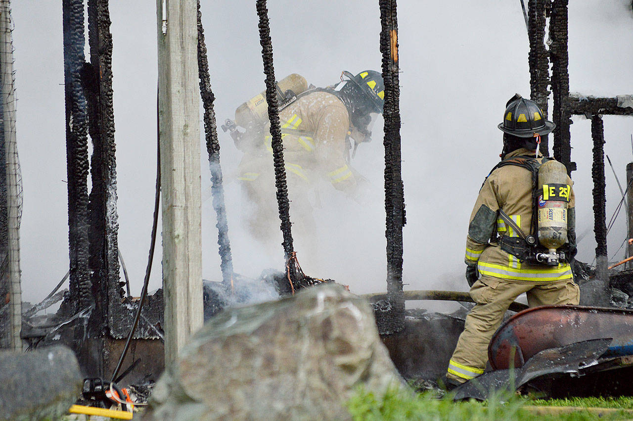 North Whidbey Fire and Rescue firefighters Dave Hanson and Stephanie Mace clear out a burning storage building Monday morning. Photo by Laura Guido/Whidbey News-Times