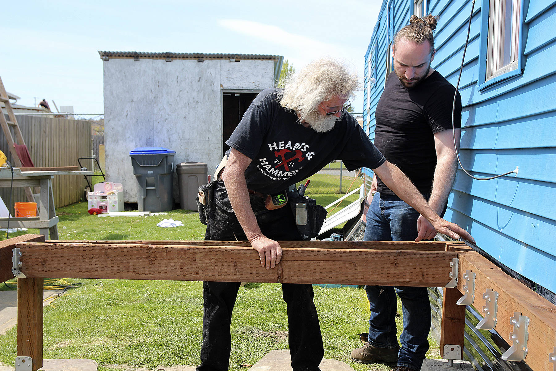 House captain is Gary Wray checks that a beam of lumber fits properly on the deck in progress as volunteer Devin Short watches. Wray is also the president of the North Whidbey Hearts & Hammers. (Photo by Maria Matson/Whidbey News-Times)