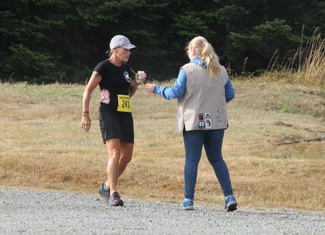 A volunteer helps a runner at a water station during last year’s Race the Reserve. More volunteers are needed to help with this summer’s event. (Photo by Jim Waller/Whidbey News-Times)