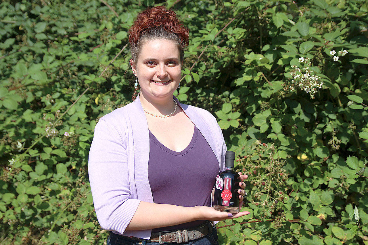Mercedes Monarch, production associate at Whidbey Island Distillery, holds a bottle of the company’s Community Batch of blackberry liqueur. It’s made using donated berries and $2 from every bottle sale go toward local nonprofits. The distillery is currently accepting blackberries for next year’s batch and will donate money for every pound collected. Photo by Laura Guido/Whidbey News Group