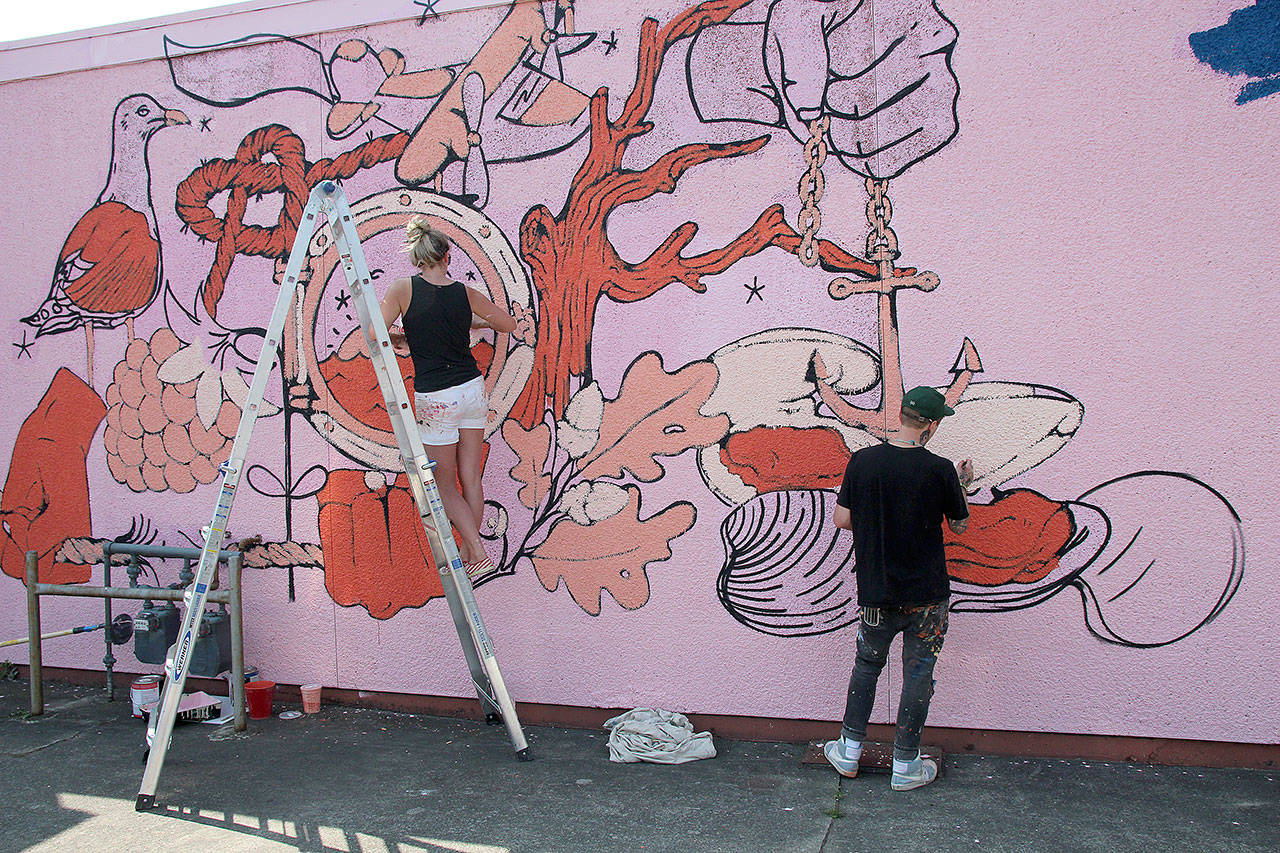 Photo by Jessie Stensland / Whidbey News-Times                                Portland artist Forest Wolf Kell and Kathleen Warren of Overall Creative work on a mural on the side of Casual House Saturday.