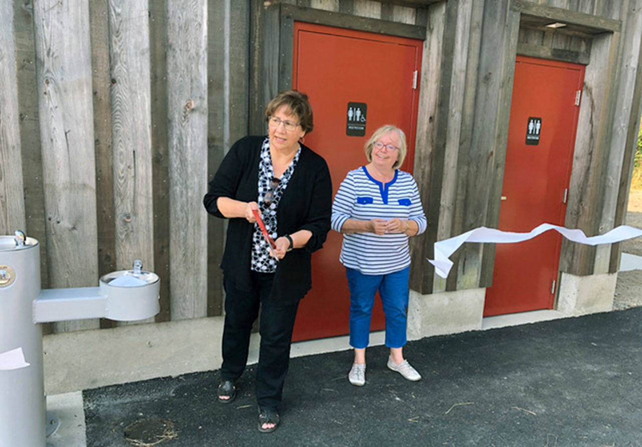 Coupeville Mayor Molly Hughes, left, joined by Coupeville Chamber Executive Director Lynda Eccles, cuts a “ceremonial” ribbon of toilet paper on Saturday Aug. 3 to officially open four new public restrooms in the parking lot at the Town Green.                                The restrooms were constructed inside the historic Holbrook Barn, which had been moved to the Town Green.                                The restroom project plus repaving and enlarging of the parking lot were paid for with county and other grants. The mayor told the gathering she was proud the entire project had come in on budget and ahead of schedule. (Photo by Harry Anderson)