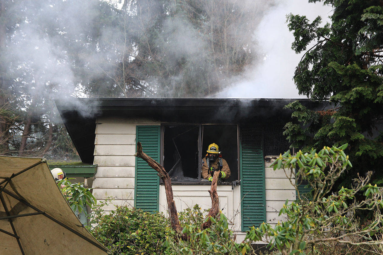 A firefighter looks out the shattered window of a home damaged by fire Friday. Photo by Laura Guido/Whidbey News-Times