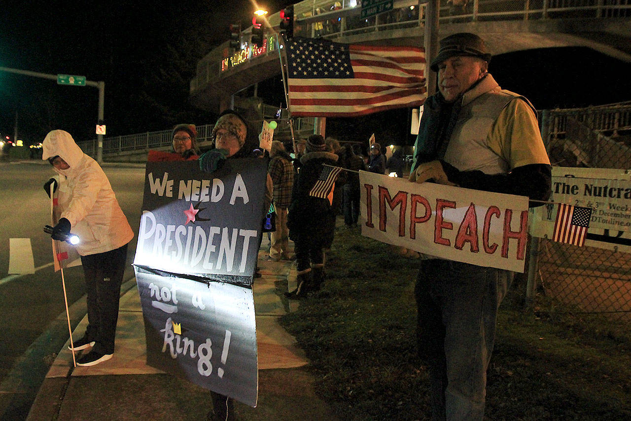 From left, Debbie Lagasse, Linda Bainbridge and Eric Tremblay join a rally Tuesday in Coupeville in support of impeachment of President Donald Trump. Below, Heide Horeth of Coupeville holds a lighted sign on the pedestrian walkway overhead. Photos by Laura Guido/Whidbey News-Times