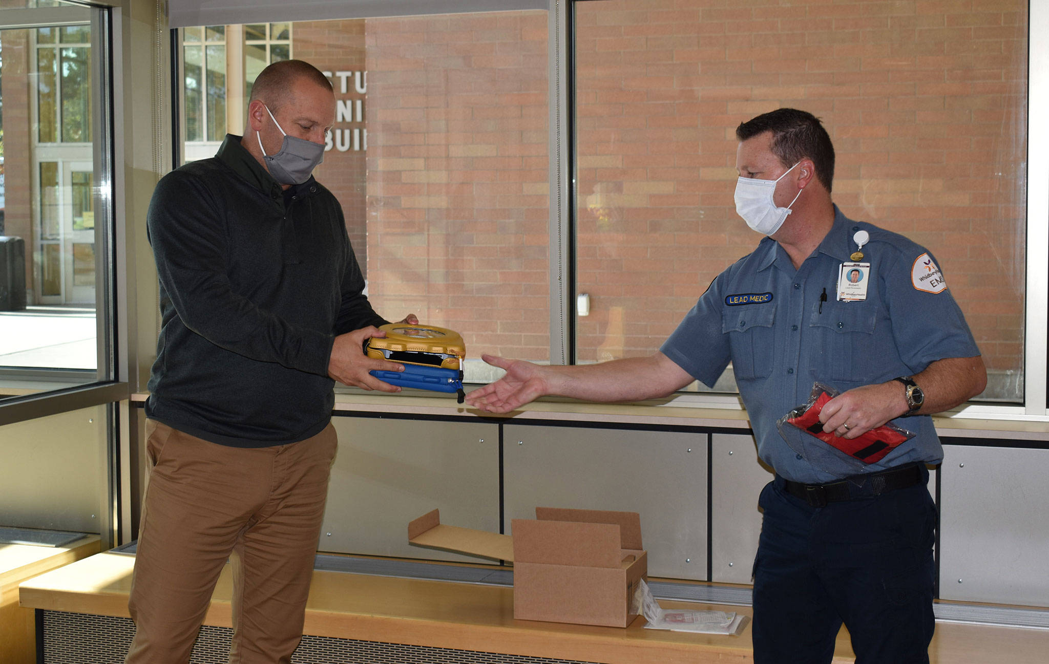 Oak Harbor High School Athletic Director Jerrod Fleury, left, receives a donated AED from Robert May, lead paramedic/public education coordinator for Whidbey Health EMS. (Photo by Tabetha Darrow)