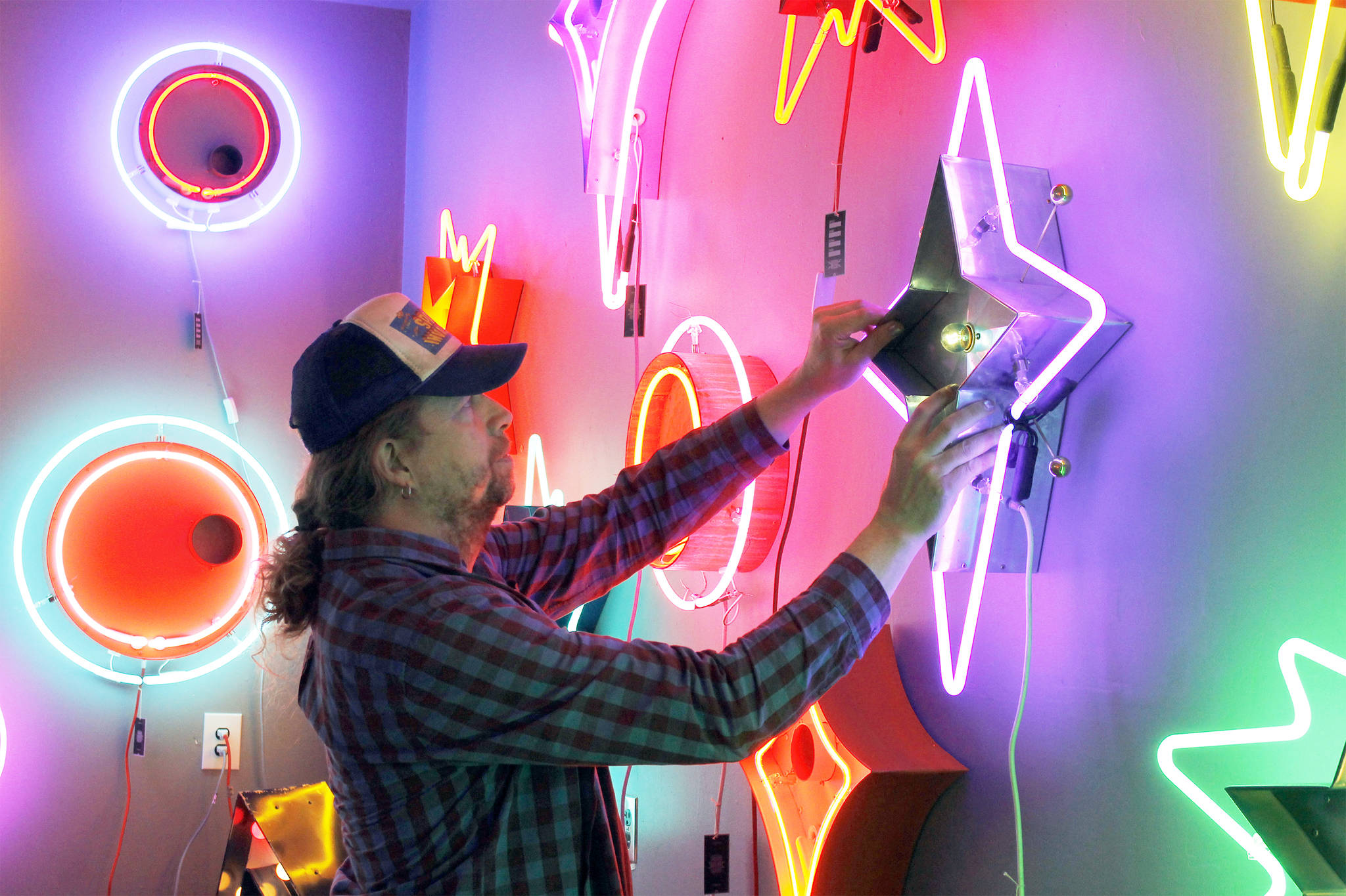 Tim Leonard, owner of the Machine Shop in Langley, hangs a purple neon star he made on the wall of his arcade. Photo by Kira Erickson/Whidbey News Group
