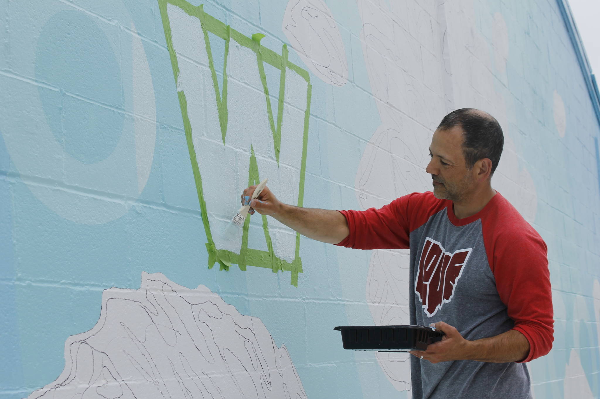 Artist Jeremy Jarvis paints words on his new mural in Langley. (Photo by Kira Erickson/Whidbey News-Times)