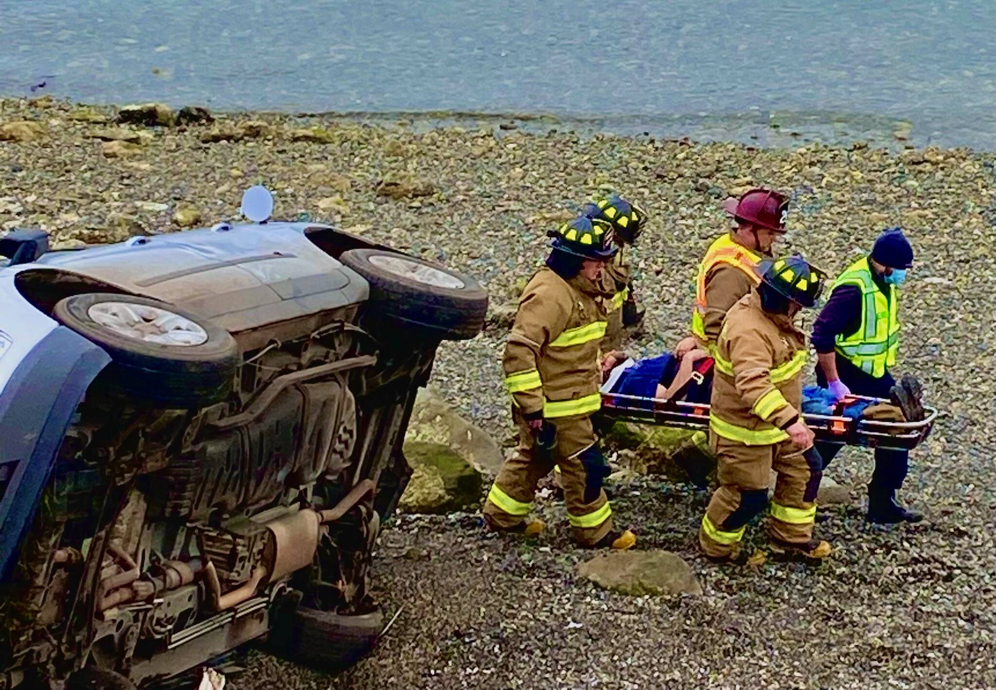 Firefighters carry a driver from the scene of a vehicle accident after the driver rolled his car near Penn Cove. (Photo provided)