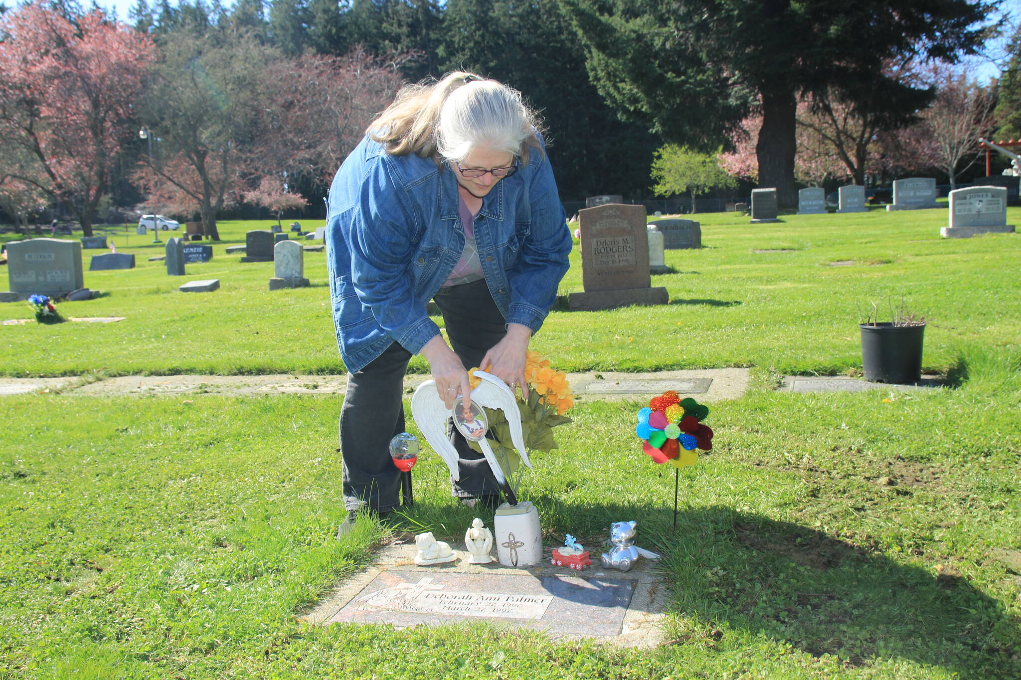Mirria Gonzalez places ceramic angel wings on Deborah Palmer’s grave. She said she occasionally finds evidence that other people have also visited the site. (Photo by Jessie Stensland/Whidbey News-Times)