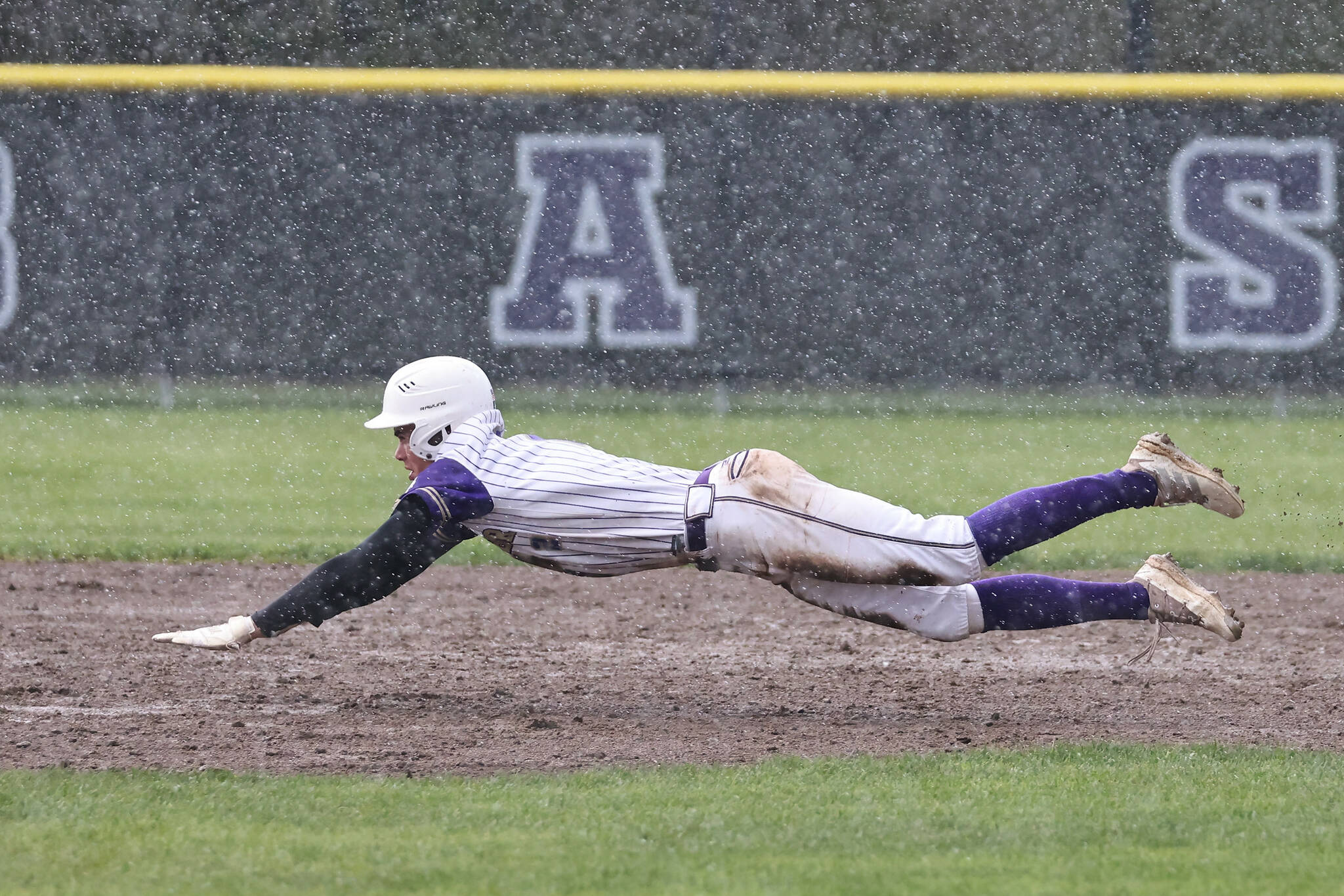 Photo by John Fisken
Oak Harbor High School baseball player Gage McLeod dives for the base during a rainy game against Anacortes April 4. Despite adverse weather conditions, the Wildcats were victorious.