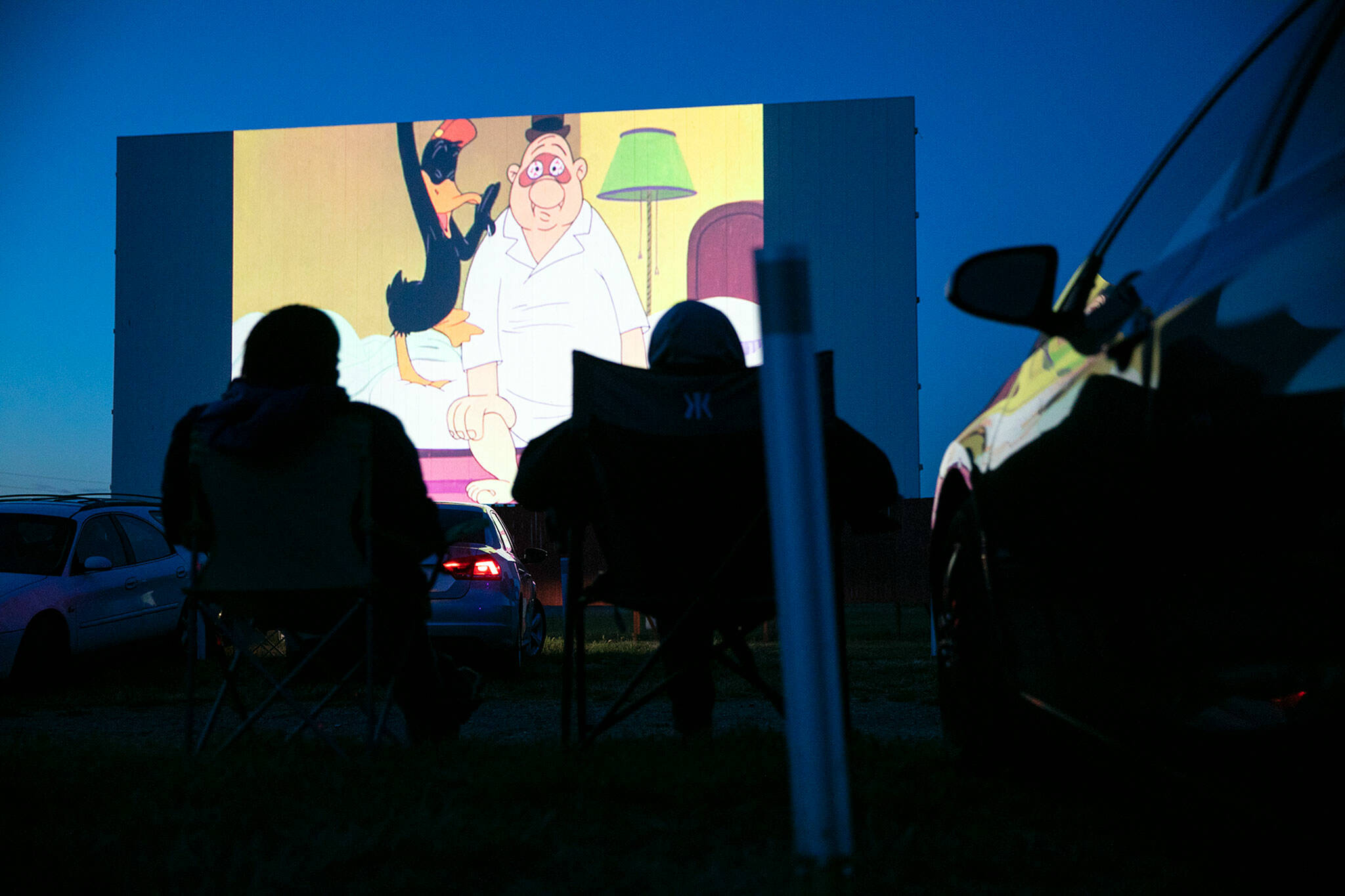 People sit in lawn chairs and watch a Looney Tunes short at the Blue Fox Drive-In Theater in Oak Harbor. (Ryan Berry / The Herald)