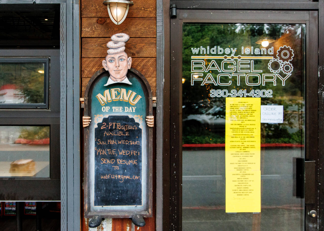Whidbey Island Bagel Factory has closed its Clinton location to retail operations. A bright yellow sign on the door tells the full story, right next to the hiring ad on the chalkboard. (Photo by David Welton)