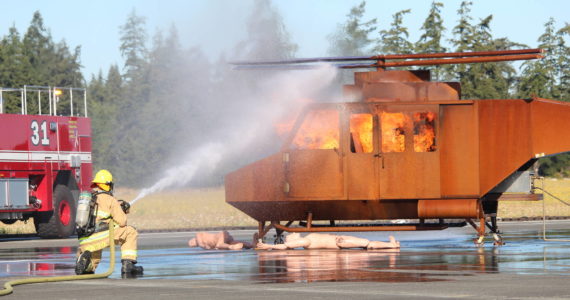 Photo by Karina Andrew/Whidbey News-Times
A Navy firefighter aims a hose at a helicopter fire during an emergency simulation at Outlying Field Coupeville Aug. 17.