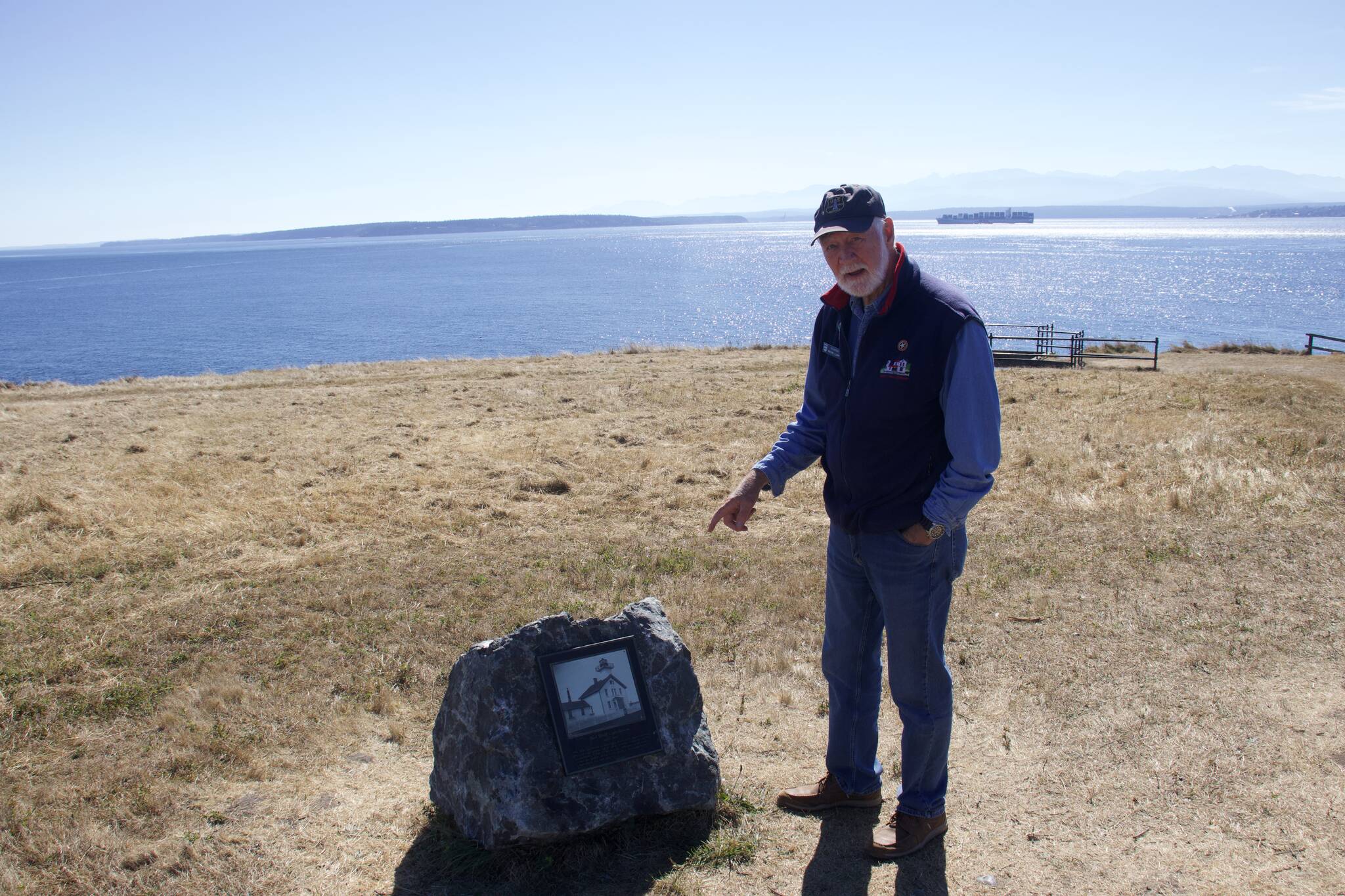 Wayne Clark, a volunteer docent at Fort Casey State Park, stands next to the the new boulder and plaque that marks the spot of the original lighthouse at Admiralty Head. (Photo by Rachel Rosen/Whidbey News-Times.)