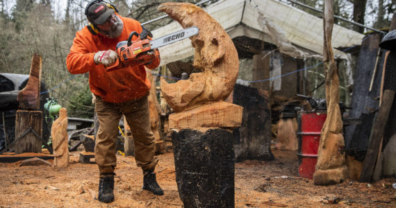 Steve Backus works on the details of a moon carving at his outdoor workshop in Clinton. A Dec. 2 fire destroyed his studio in the former sawmill on the 4-acre Glendale Road property that houses his Big Shot Woodcarving business and home. (Olivia Vanni / The Herald)